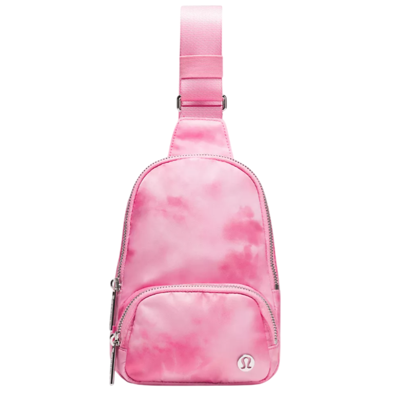 A small pink sling bag with a tie-dye pattern, featuring a front zippered pocket and an adjustable strap. The brand logo is visible on the front of the bag.