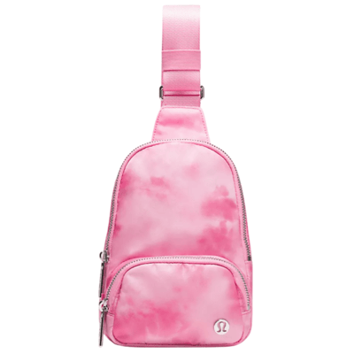 A small pink sling bag with a tie-dye pattern, featuring a front zippered pocket and an adjustable strap. The brand logo is visible on the front of the bag.