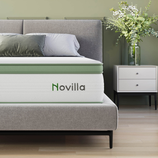 A gray bed with a green-accented Novilla mattress is shown alongside a white nightstand with a vase of green and white flowers.