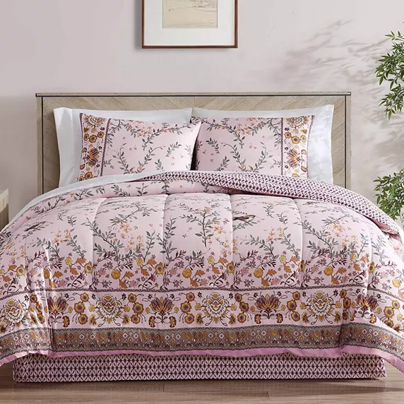 The 8pc Triliana Soft Pink Comforter Set features a floral and geometric pattern in soft pink, yellow, and purple tones. It includes a comforter, two pillow shams, two Euro shams, a flat sheet, a fitted sheet, and a decorative pillow.