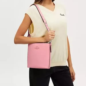 A person wearing a sleeveless top and black pants, carrying a pink shoulder bag with a strap.