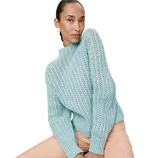A model wearing a light blue, textured knit sweater paired with peach pants.