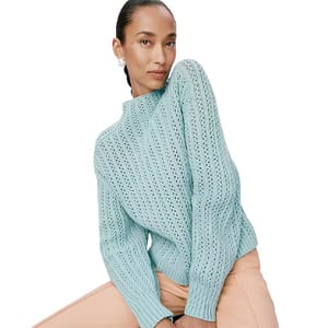 A model wearing a light blue, textured knit sweater paired with peach pants.