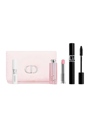 A cosmetic set includes a white serum bottle, pink lip balm, black mascara, and a light pink pouch with a metallic clasp.
