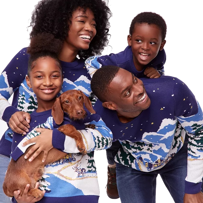 A family of four, including a dog, wears matching blue and white winter-themed sweaters, showcasing a cozy, coordinated holiday look.