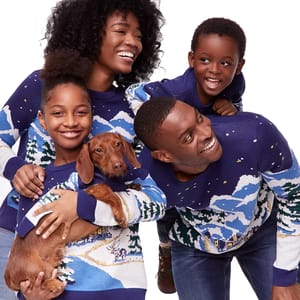 A family of four, including a dog, wears matching blue and white winter-themed sweaters, showcasing a cozy, coordinated holiday look.
