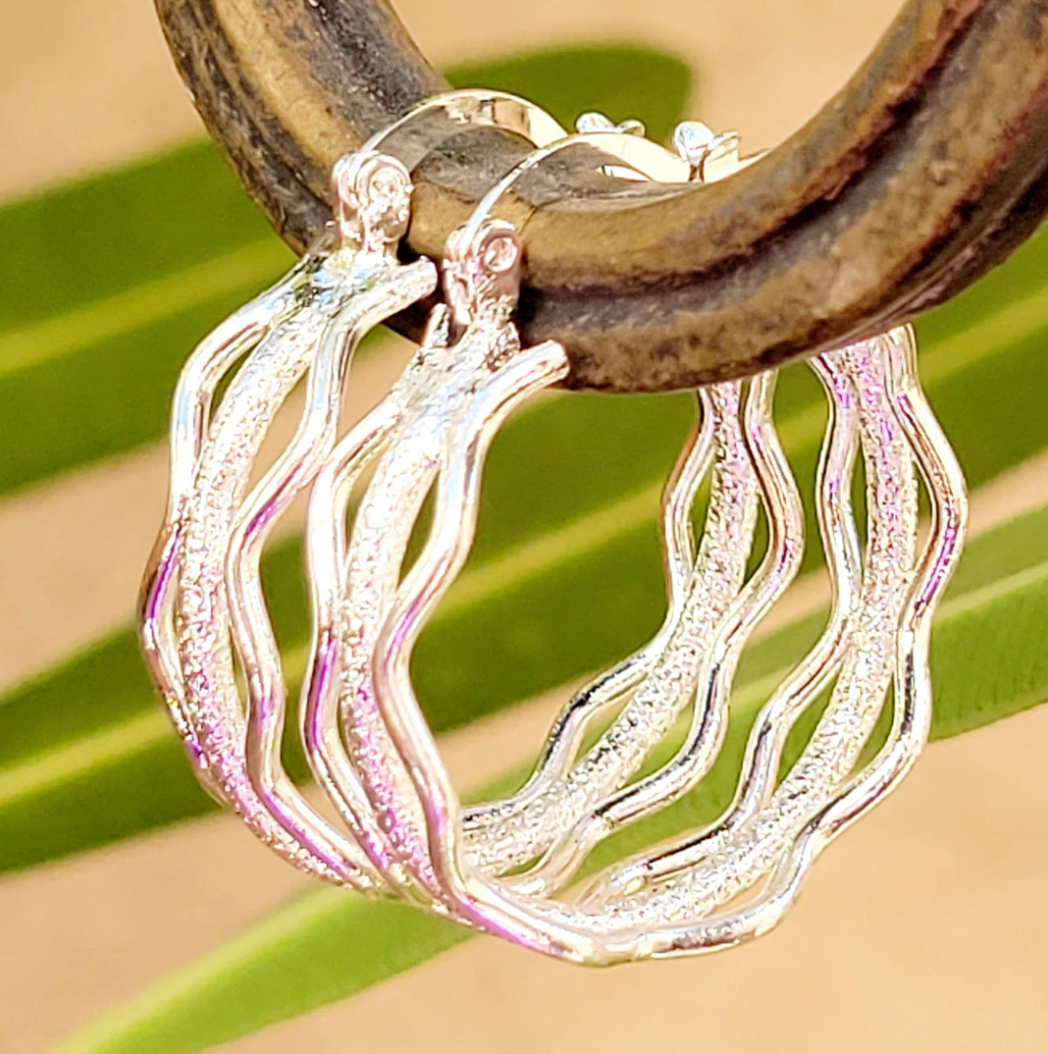 Silver hoop earrings with a wavy design hanging on a rustic wooden surface.