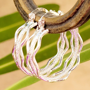 Silver hoop earrings with a wavy design hanging on a rustic wooden surface.