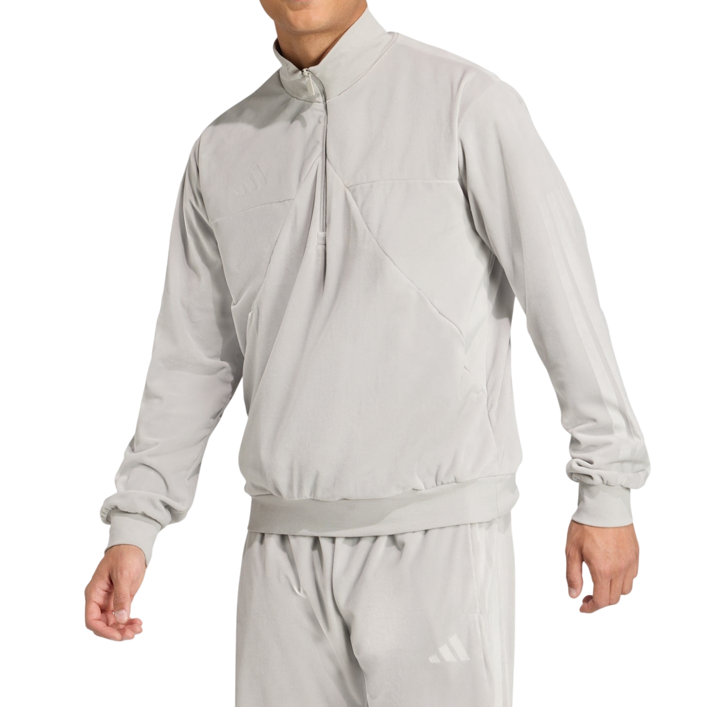 A person is wearing a light grey, long-sleeved tracksuit with a high collar, featuring subtle branding on the chest and leg.