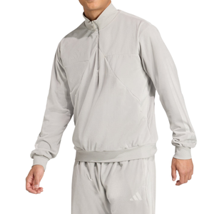A person is wearing a light grey, long-sleeved tracksuit with a high collar, featuring subtle branding on the chest and leg.