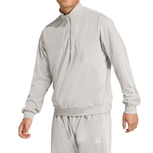 A person is wearing a light grey, long-sleeved tracksuit with a high collar, featuring subtle branding on the chest and leg.