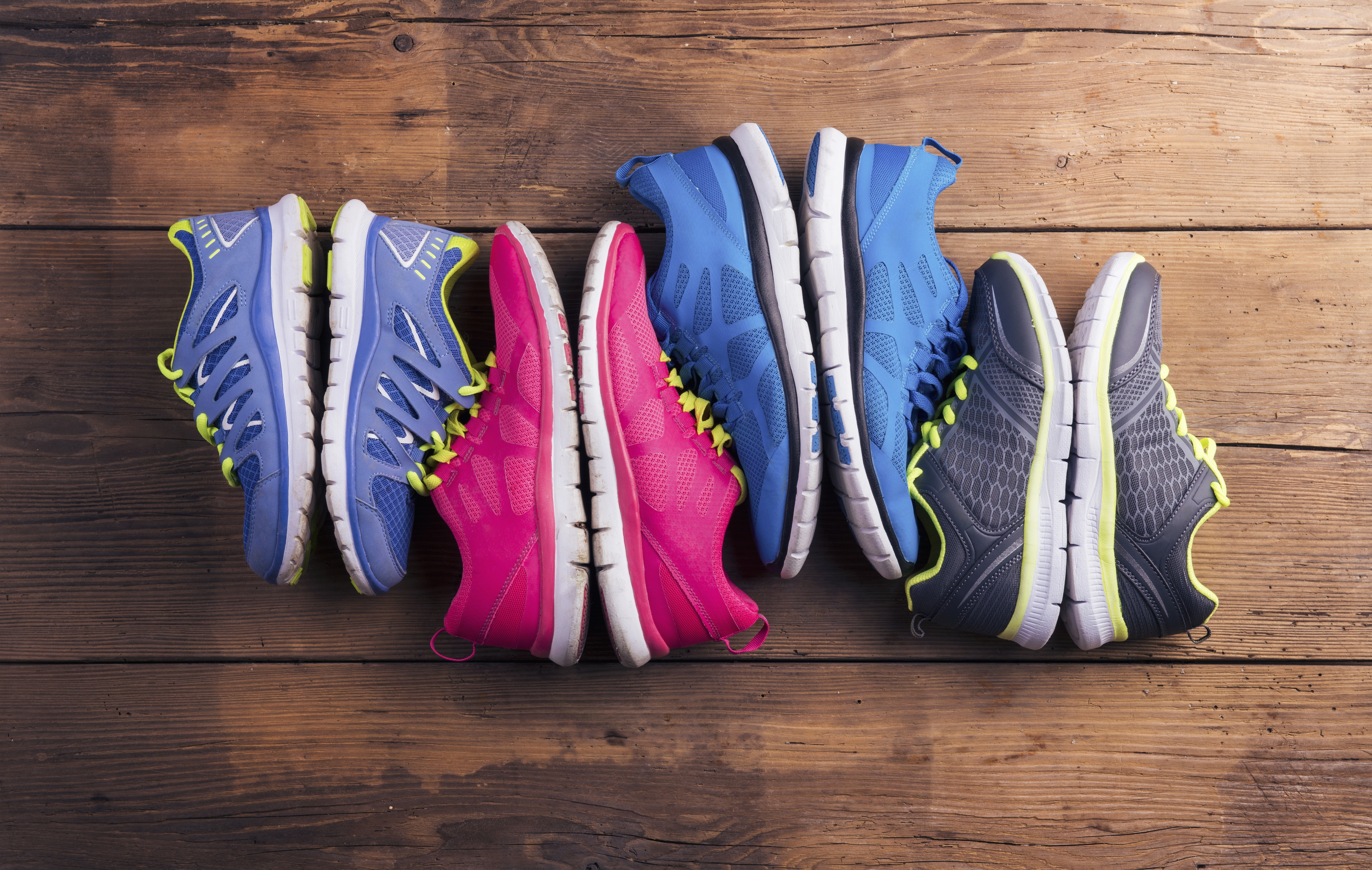Three pairs of athletic shoes in blue, pink, and gray on a wooden floor.