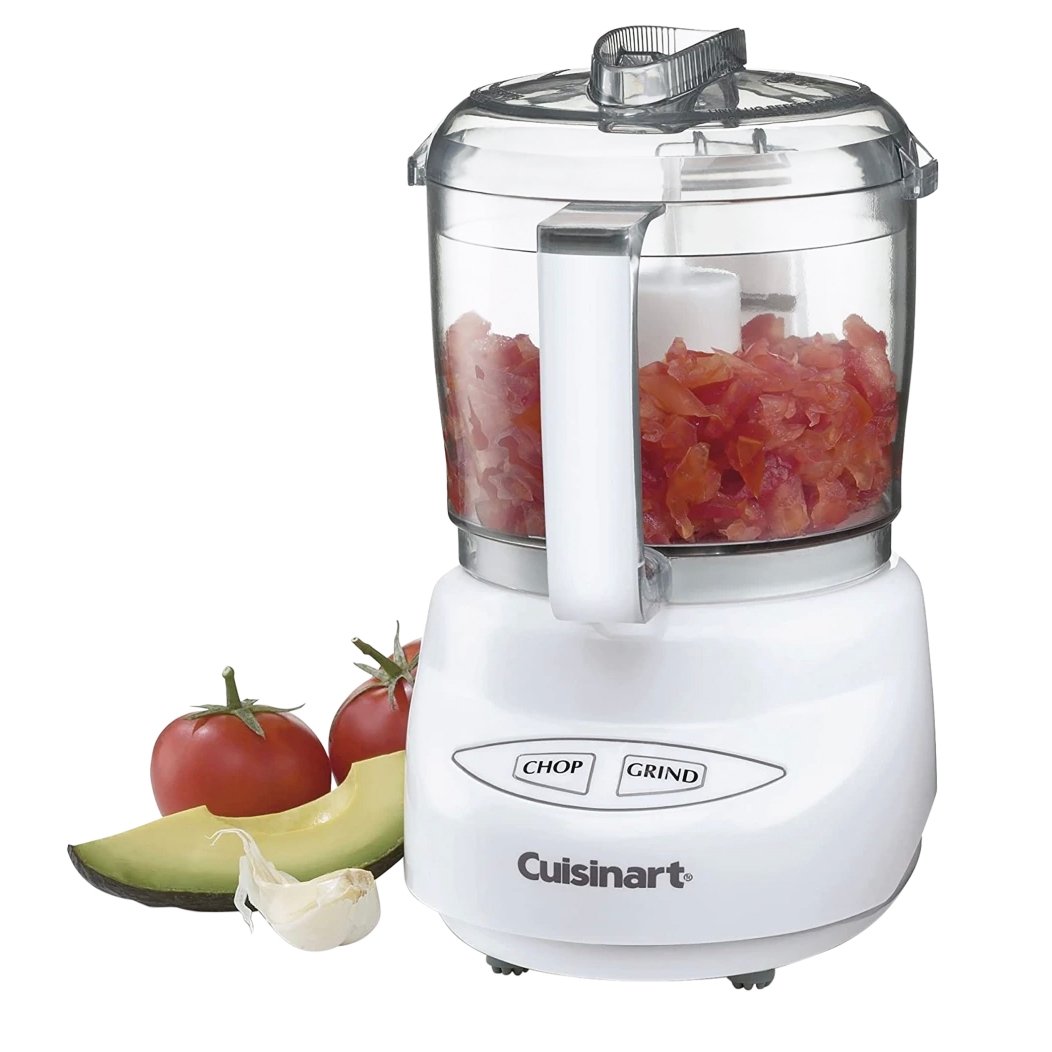 Cuisinart mini food processor with \“Chop\“ and \“Grind\“ functions. Chopped tomatoes are inside the container, surrounded by whole tomatoes, half an avocado, and garlic cloves.