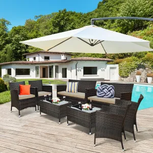 Outdoor patio set with dark wicker chairs, sofas, and glass-top tables featuring cushions and colorful pillows, set on a deck by a swimming pool with a large umbrella.