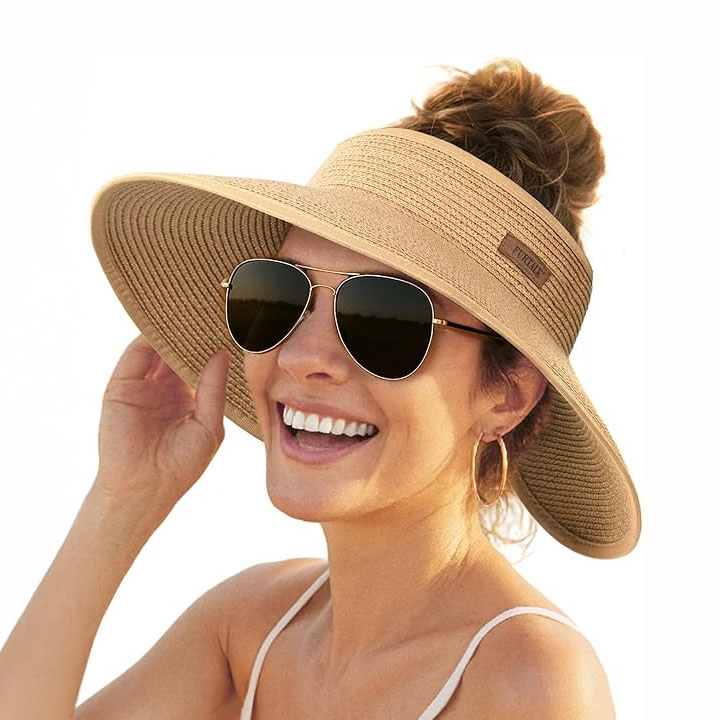 Wide-brimmed sun visor hat in a light tan color, with a strap for securing, worn by a woman with sunglasses and hoop earrings.
