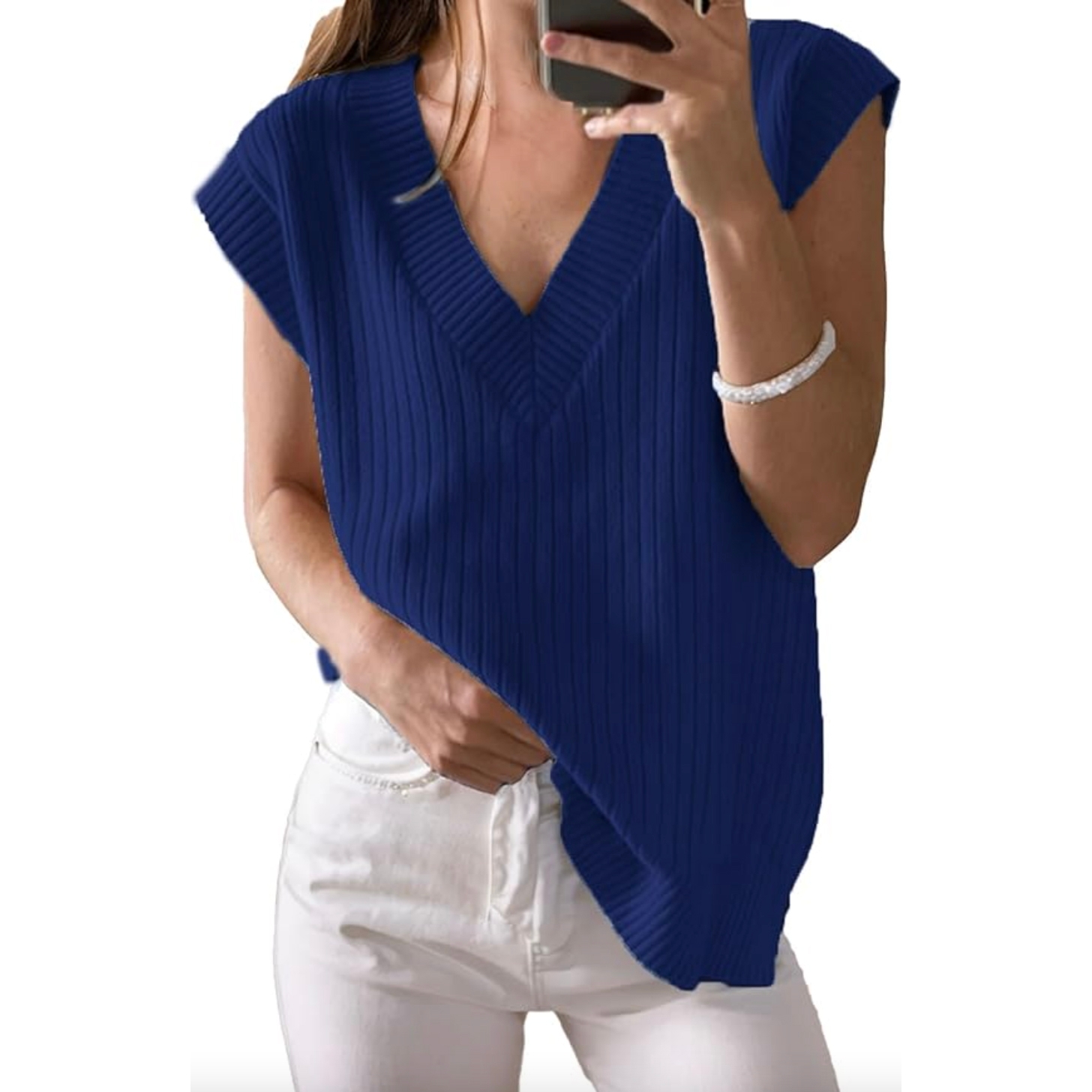 A woman wearing a blue sleeveless ribbed V-neck sweater paired with white pants and a bracelet. She is holding a phone in one hand.