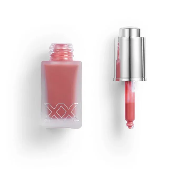 A pink liquid cosmetic in a frosted glass bottle with \“XX\“ branding and a metallic dropper lid beside it.