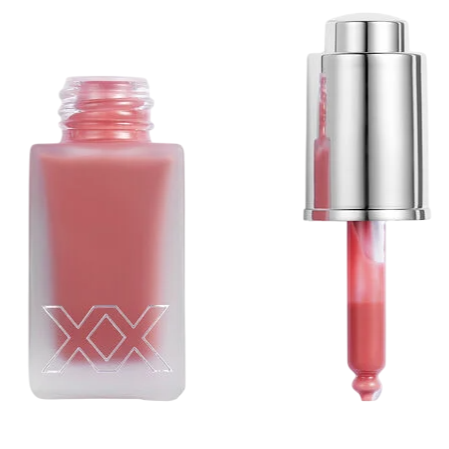 A pink liquid cosmetic in a frosted glass bottle with \“XX\“ branding and a metallic dropper lid beside it.