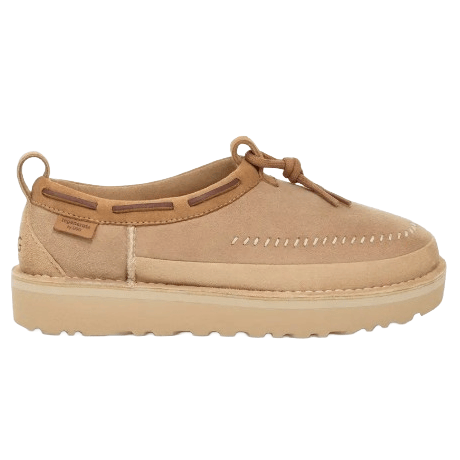 A tan suede moccasin-style shoe with stitching details, a thick sole, and lace closures at the top, featuring a loop on the back for easy wear.