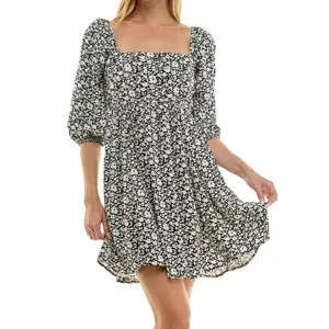 A woman is wearing a black and white floral dress with a square neckline and puffed three-quarter sleeves. The dress has a loose, flowing fit.