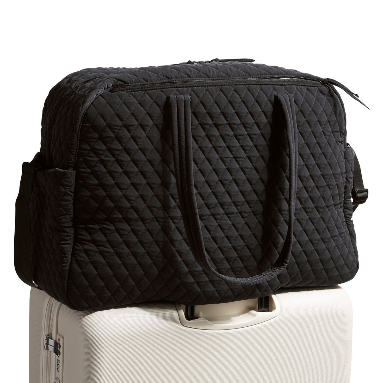 A black quilted travel duffel bag is placed on top of a white rolling suitcase.