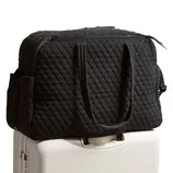 A black quilted travel duffel bag is placed on top of a white rolling suitcase.