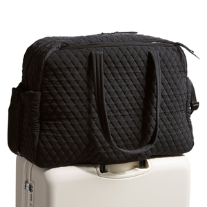 A black quilted travel duffel bag is placed on top of a white rolling suitcase.