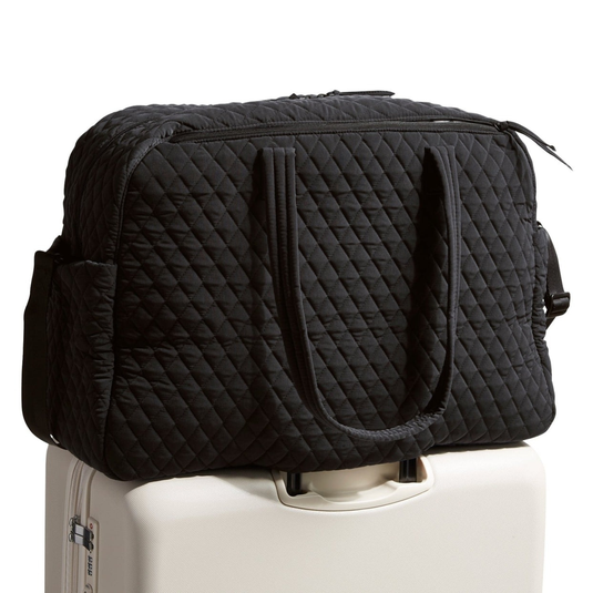 A black quilted travel duffel bag is placed on top of a white rolling suitcase.