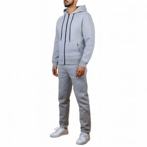 A person is wearing a light gray hoodie with a front zipper and drawstrings, matching jogger pants, and white low-top sneakers.