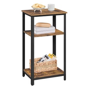 A three-tier storage end table with a rustic wood finish and black metal frame. The top shelf holds a bowl with cookies and a mug, the middle has books and a box, and the bottom has a wicker basket with items inside.