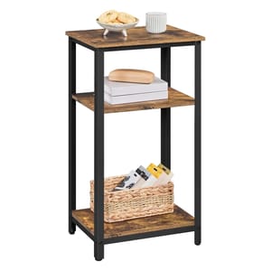 A three-tier storage end table with a rustic wood finish and black metal frame. The top shelf holds a bowl with cookies and a mug, the middle has books and a box, and the bottom has a wicker basket with items inside.