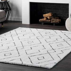 A white rug with a black geometric pattern is placed on a dark wood floor in front of a fireplace with logs.