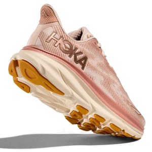 Hoka running shoe in a pink and beige color scheme, featuring a thick sole with orange and beige outsole accents.