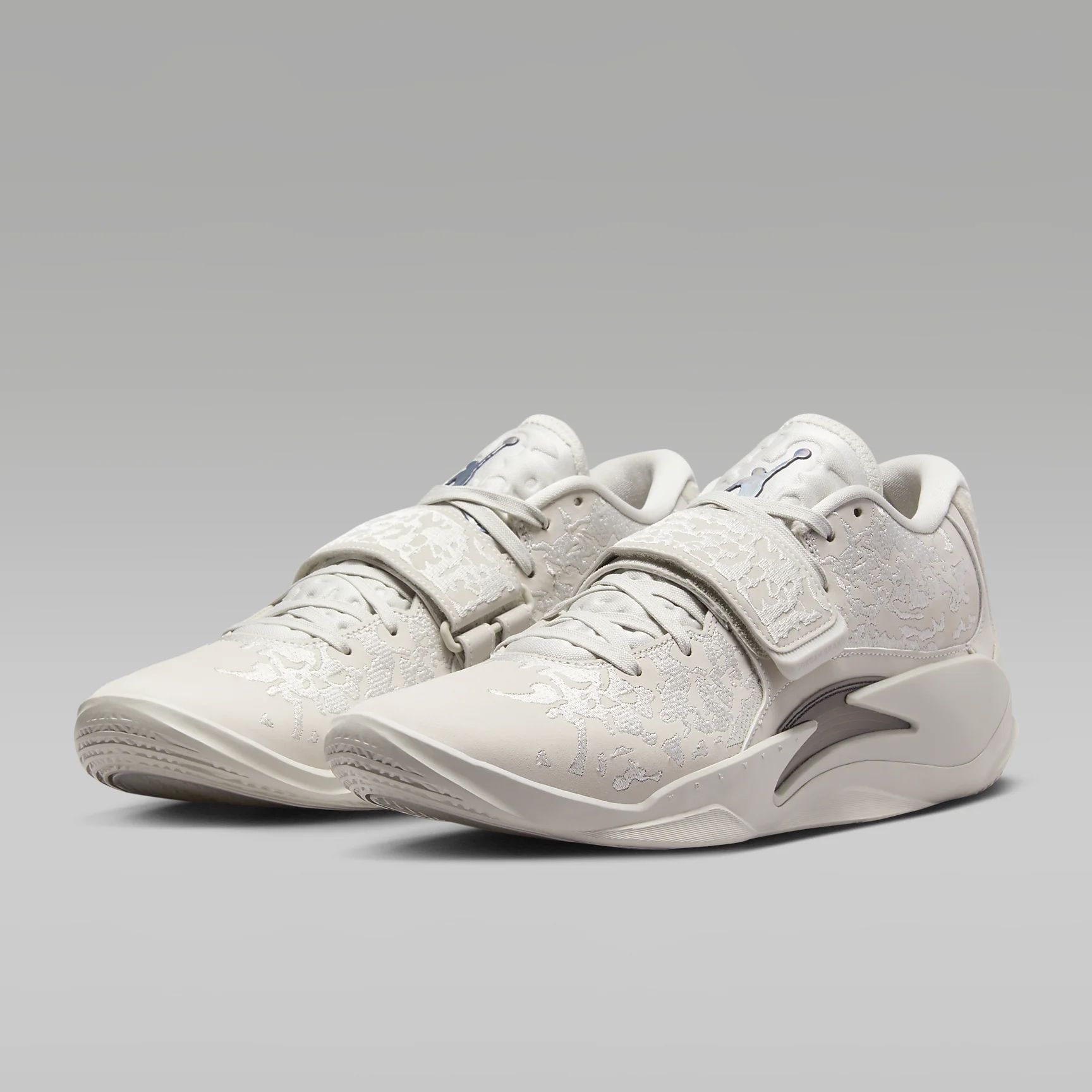 A pair of cream-toned sneakers with embossed detailing and a swoosh-like emblem on the side.