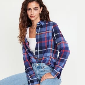 A woman is wearing a blue and red plaid shirt with a white top underneath and light blue jeans.