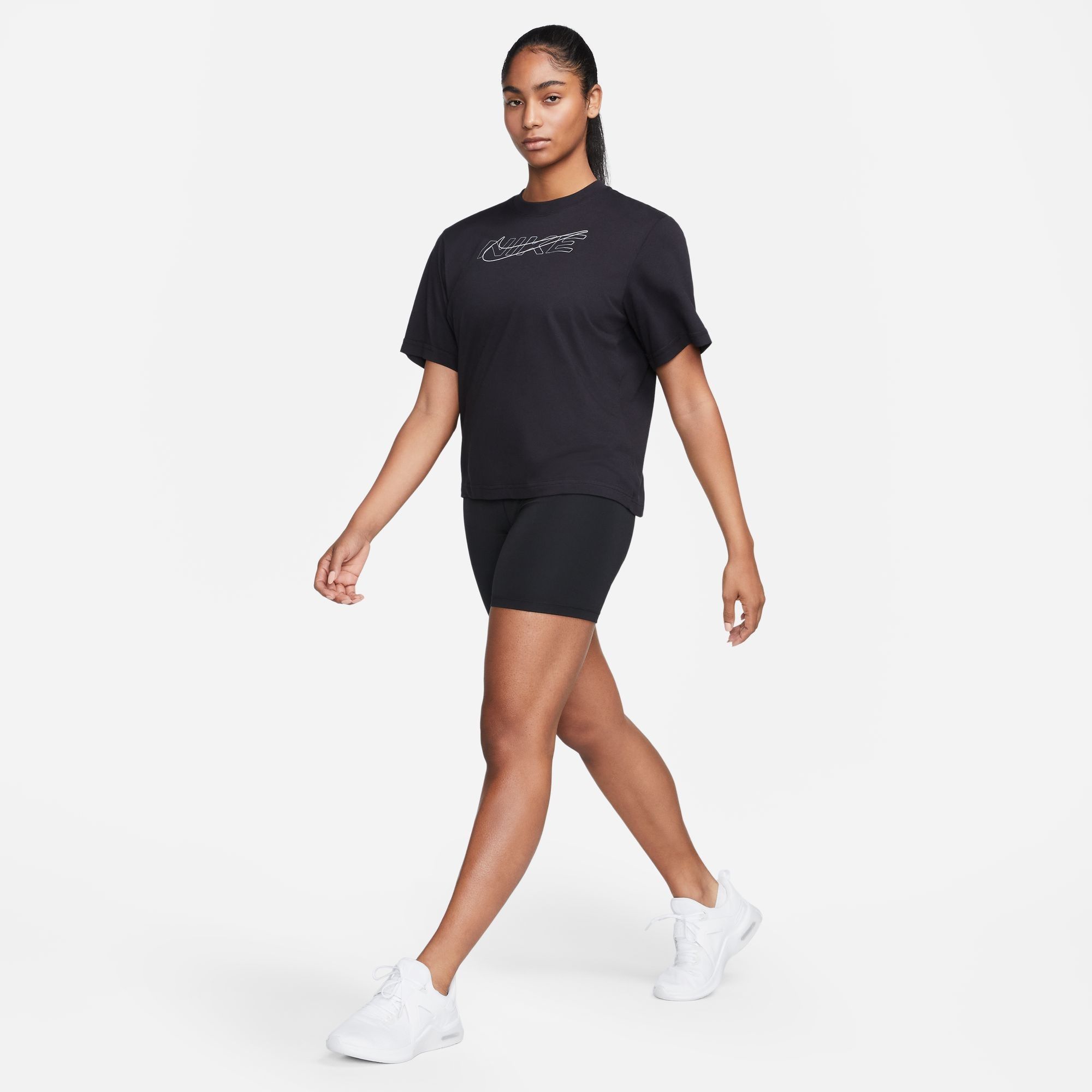 A woman is wearing a black crew neck T-shirt, black shorts, and white sneakers.