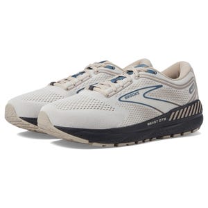 A pair of Brooks Beast GTS 23 running shoes with a light beige upper, white mesh, and navy and light blue accents, featuring a thick sole for support.