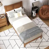 A cozy bedroom setup with a wooden bed frame, layered bedding, and several decorative pillows. Nearby, a guitar and amp are placed alongside a leather bean bag chair, and geometric-patterned rugs cover the floor.