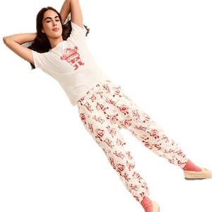 Woman in casual sleepwear: a white T-shirt with a red robot design, white pajama pants with red patterns, pink socks, and beige slippers.