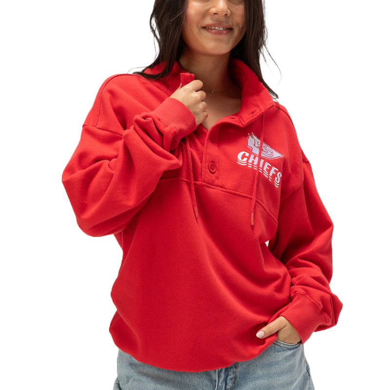 A person wears a red pullover with a collar, featuring the word \“CHIEFS\“ and a logo, paired with light blue jeans.
