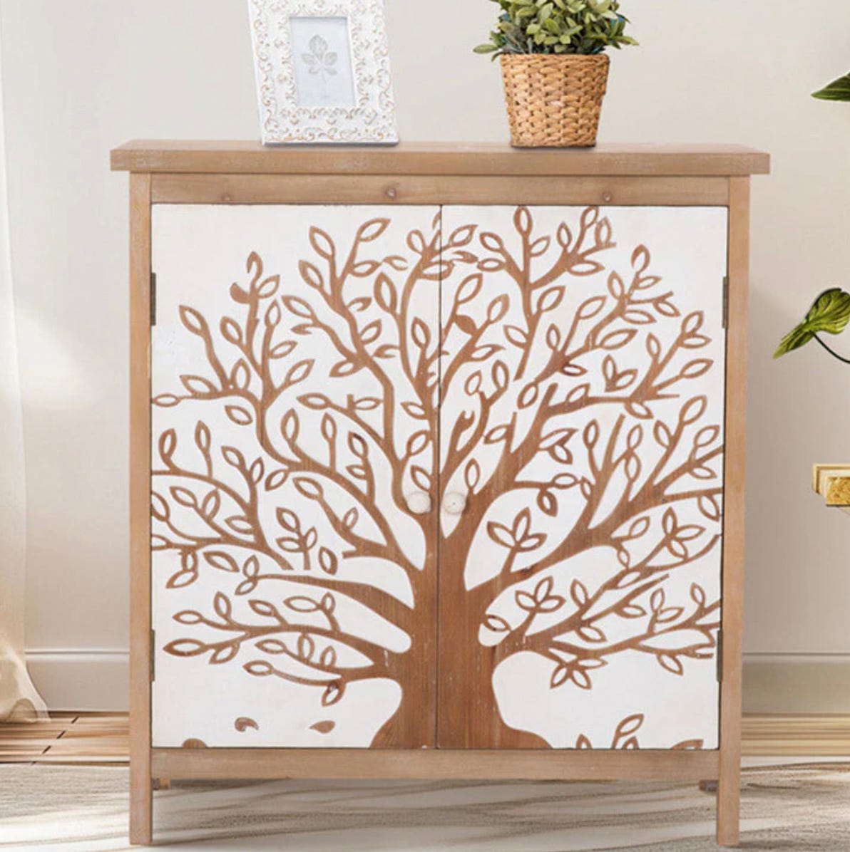 Wooden cabinet with tree design on the doors, topped with a photo frame and potted plant for home decor.