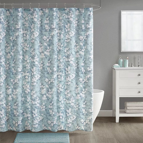 A bathroom set featuring a floral-patterned shower curtain with matching accessories in shades of blue and white. The set includes a bath mat, toothbrush holder, soap dispenser, and a small towel, coordinating with the overall color scheme.
