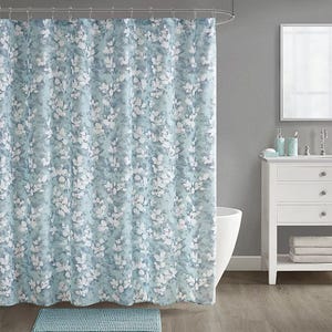 A bathroom set featuring a floral-patterned shower curtain with matching accessories in shades of blue and white. The set includes a bath mat, toothbrush holder, soap dispenser, and a small towel, coordinating with the overall color scheme.