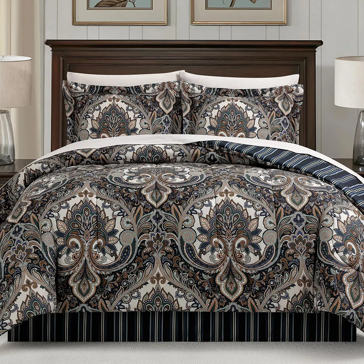 A bed with a paisley-patterned comforter and matching pillow shams in dark and light tones, complemented by a striped bed skirt in similar colors, and flanked by two table lamps.