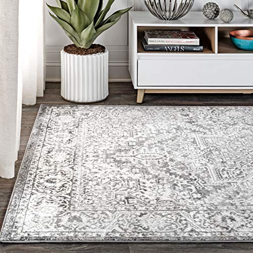 A distressed grey and white medallion rug is partially laid out, with its edge under a white bookshelf adorned with decor items and books.