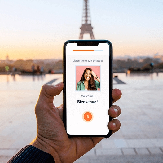 A smartphone displaying a language learning app with the Eiffel Tower in the background.