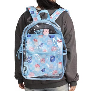 A transparent backpack with blue trim and cartoon animal patterns, featuring \“Squish Squad\“ text and a detachable keychain charm, worn by a person in a dark hoodie.