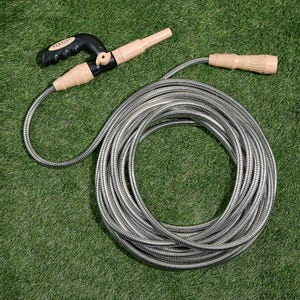 50' expandable metal hose with a durable coiled design, beige nozzle, and black handle for easy grip, suitable for various watering needs on grass or garden areas.