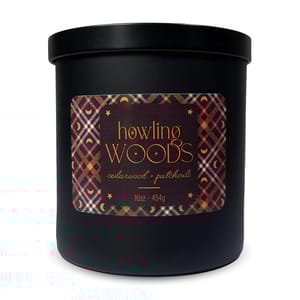 A black candle labeled \“howling WOODS\“ scented with cedarwood and patchouli, 16oz (454g), features an orange and black geometric pattern and moon design on the label.