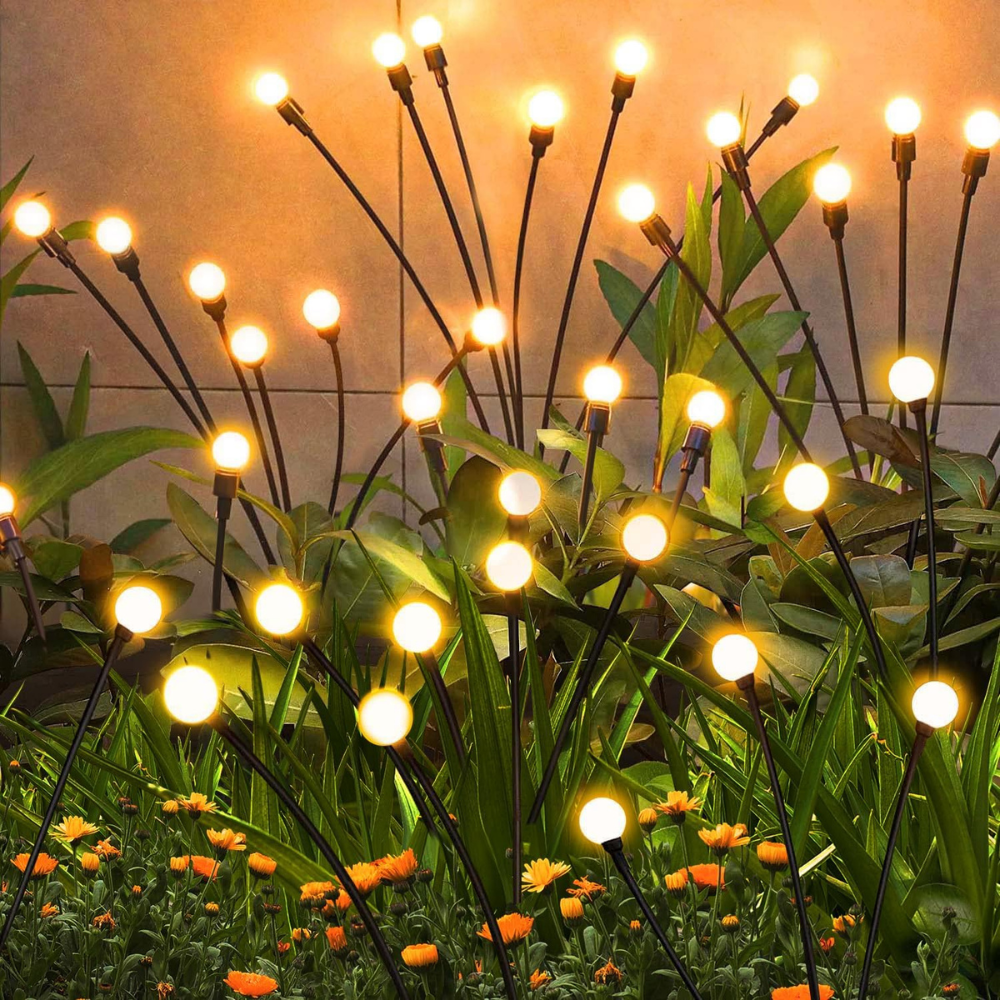 Solar-powered garden stake lights with warm white LED bulbs, resembling glowing flowers, are surrounded by various plants and colorful marigolds.